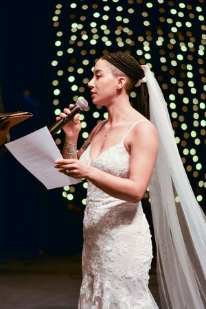 Bride reading from paper during wedding speech with twinkle lights in background.