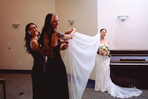 A wedding dress is held up in front of a piano while someone stands behind it in a dark room.