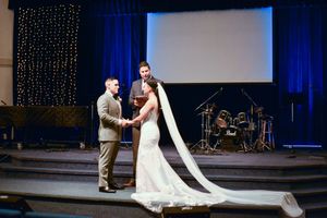A wedding ceremony takes place on a stage with elegant blue lighting and white curtains.