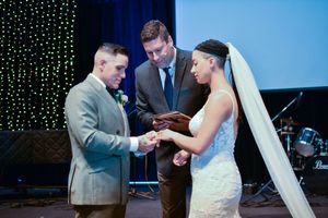 Exchange of rings during wedding ceremony with twinkle lights in background.