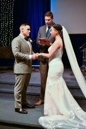 A couple exchanges rings during their wedding ceremony on a stage with blue lighting and string lights.