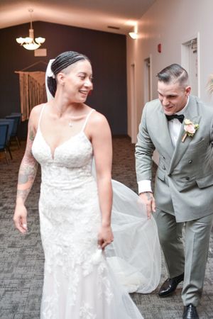 A couple shares a joyful moment in their wedding attire, with the bride in lace and groom in grey.