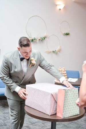 Groom in gray suit opening wedding gifts at reception.