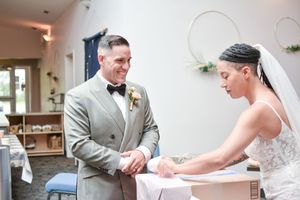 A couple signs their marriage license together at a white table during their wedding day.