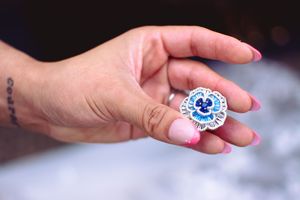 A hand holds a small round blue and white sticker with a smiley face design against a blurred background.