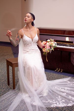 A bride in a flowing white lace gown poses gracefully next to a grand piano in an elegant indoor setting.