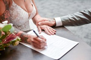 Close-up of hands signing marriage certificate with floral decor.