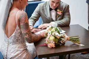 Wedding details with bouquet of peach roses and rings on wooden surface.