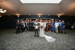 Wedding party and guests gathered for a group photo in an indoor venue.