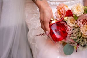 A hand pours red wine into a glass next to pink roses and soft white fabric.