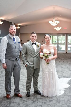Wedding party in grey suits and white dress posing together on grey carpet in reception venue.