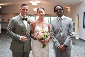 Three wedding attendees pose formally indoors with a bouquet of pink roses.