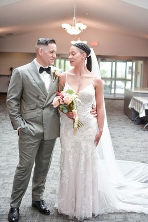 Wedding couple in formal attire poses together in an elegant indoor venue with chandeliers.
