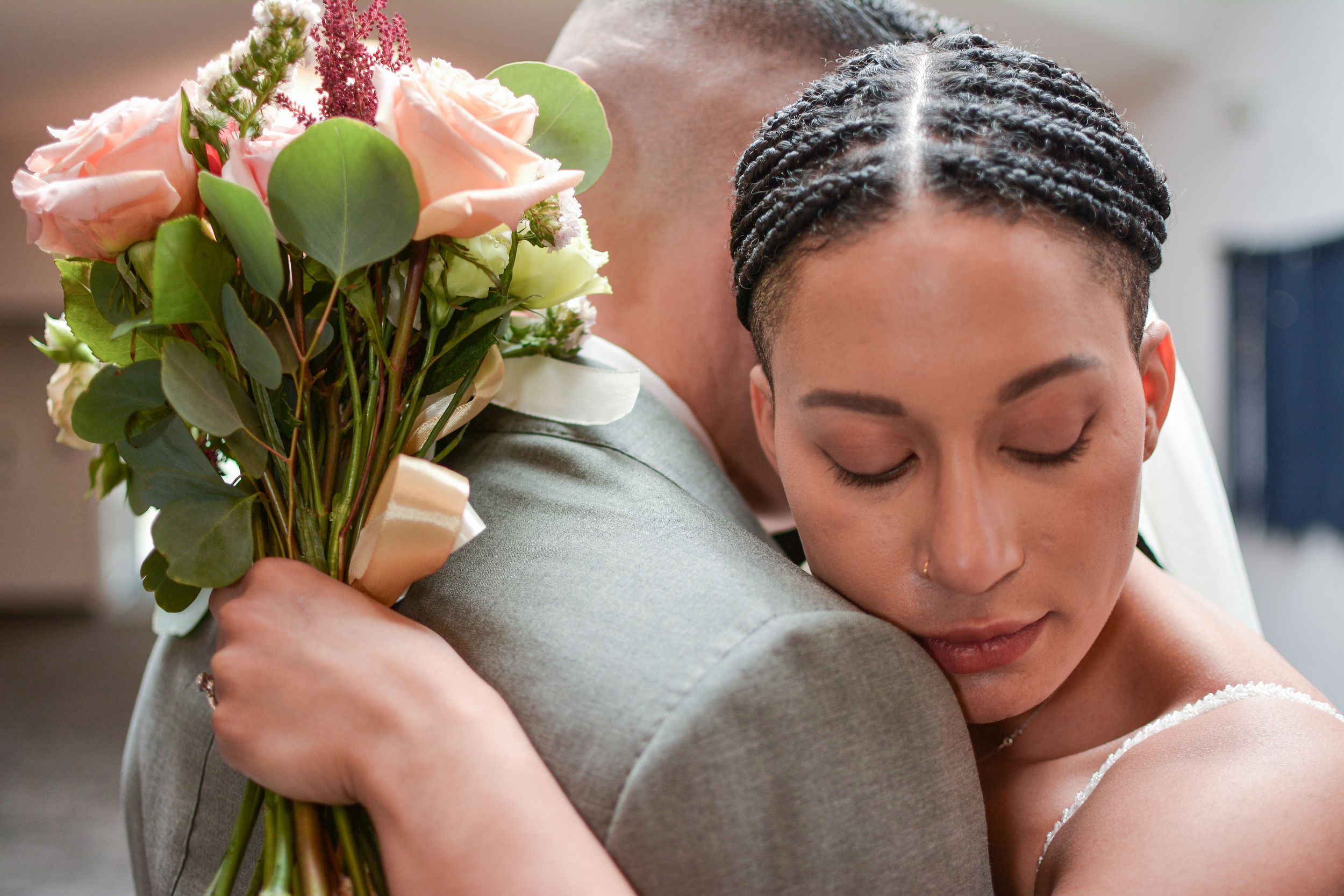 An emotional embrace captured during wedding celebrations with a peach rose bouquet.
