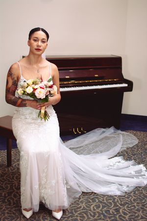 White wedding gown with delicate details positioned next to a grand piano on patterned carpet.