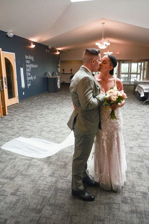 A couple in wedding attire shares their first dance together on a gray carpeted floor in an indoor venue.