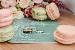 Wedding rings displayed on a mint green invitation card surrounded by delicate pink and white macarons.
