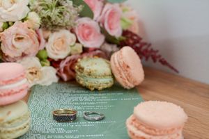 Pink and peach roses arranged with delicate macarons on a mint green surface.