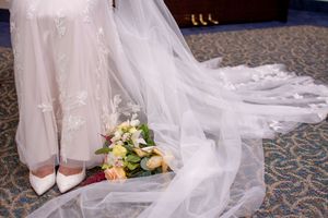 Long flowing white wedding dress train with delicate lace details trails across a textured carpet floor.