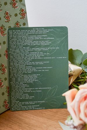 Green wedding program cards with white text displayed on a wooden surface with pink roses.