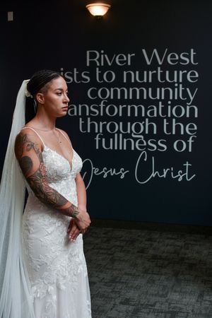 Elegant bride in lace dress stands before inspirational wall text.