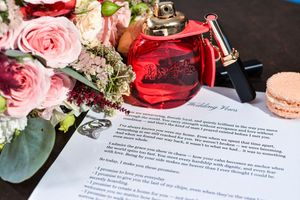 Wedding documents and paperwork laid out with pink roses and red decor on a dark surface.