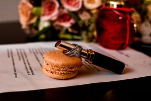 Wedding details with pink roses and macarons beside document.