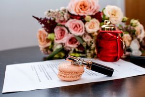 Wedding details featuring pink roses, macarons and paperwork on wooden surface.
