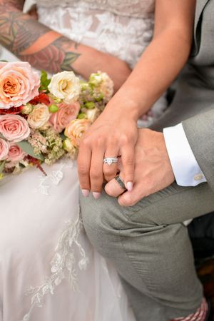 Close-up of wedding rings and hands with delicate floral bouquet.