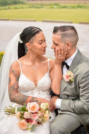A tender wedding moment with a couple sitting outdoors, featuring a beautiful bouquet of peach roses.