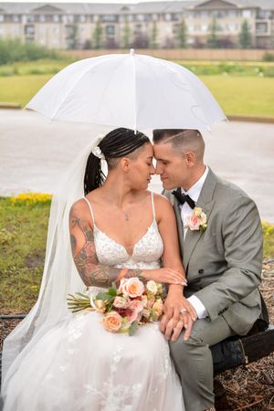 Wedding couple poses with white umbrella against apartment building backdrop.