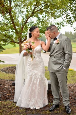 Wedding couple poses together in a natural outdoor setting with trees and mulch.