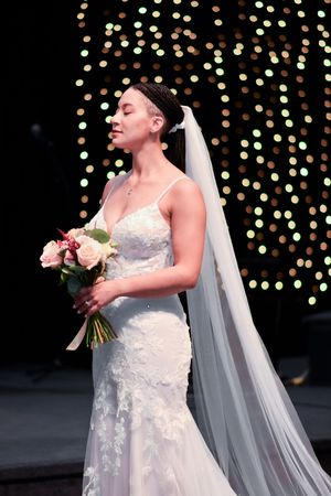 Wedding dress details with lace overlay and flowing veil against a backdrop of twinkling lights.