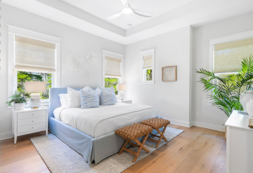 Modern coastal style bedroom interior with white walls, hardwood floors, and natural light from large windows.