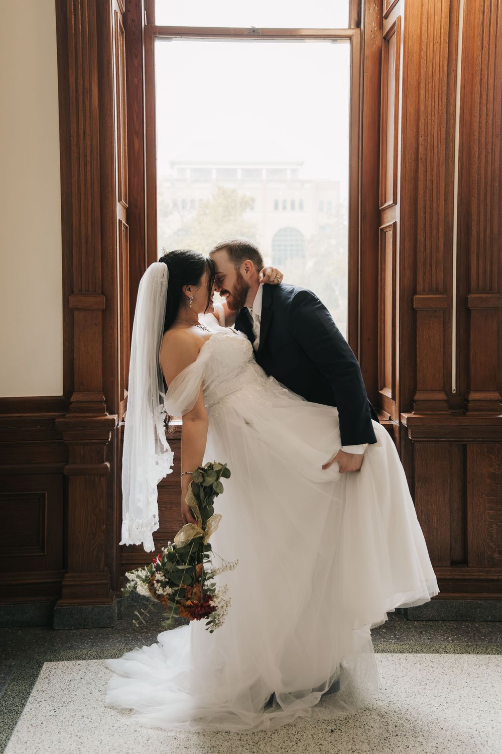 A romantic wedding couple shares intimate moments in a series of dip poses by a sunlit window with wood paneling.