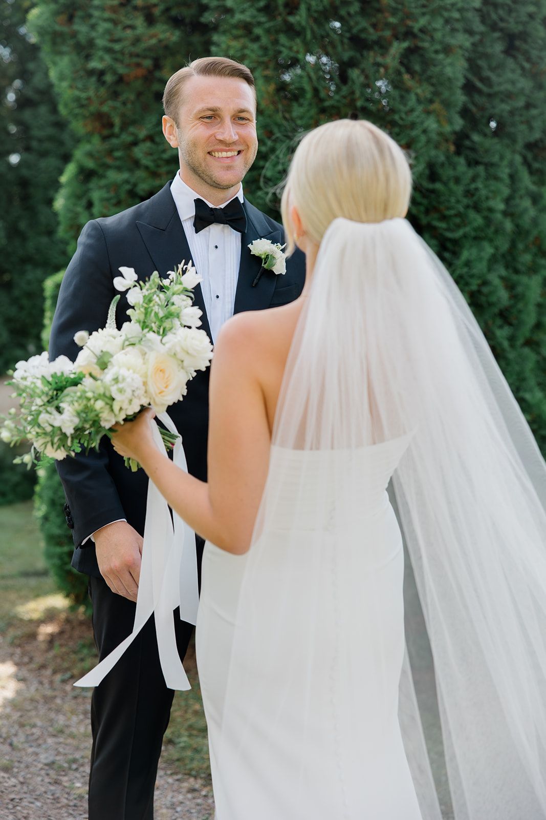 A bride and groom share their first look moment in a garden setting during their elegant outdoor wedding ceremony.