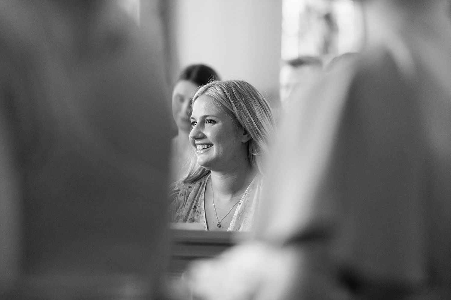 Black and white candid photograph showing a person smiling in profile view, framed between blurred foreground elements.