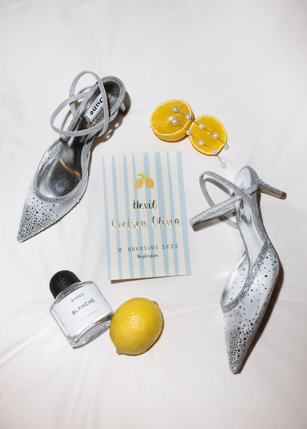 Styled flat lay of silver bridal shoes with citrus and blue striped stationery on white background.