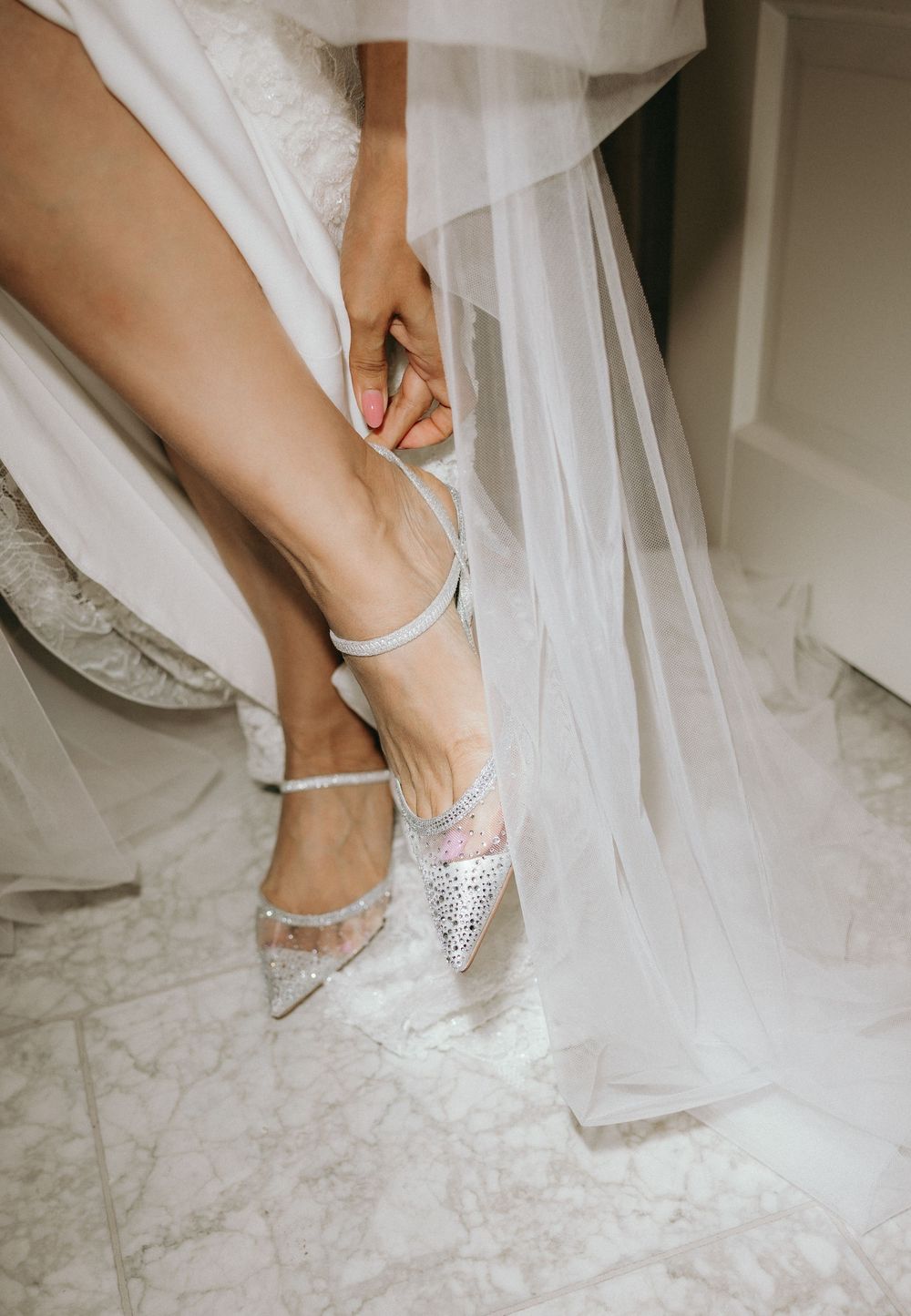 Close-up of sparkly bridal shoes being put on with flowing white dress fabric.