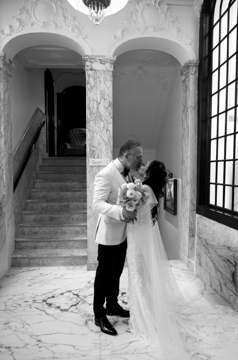Black and white wedding photos captured in a grand marble foyer with arched windows.