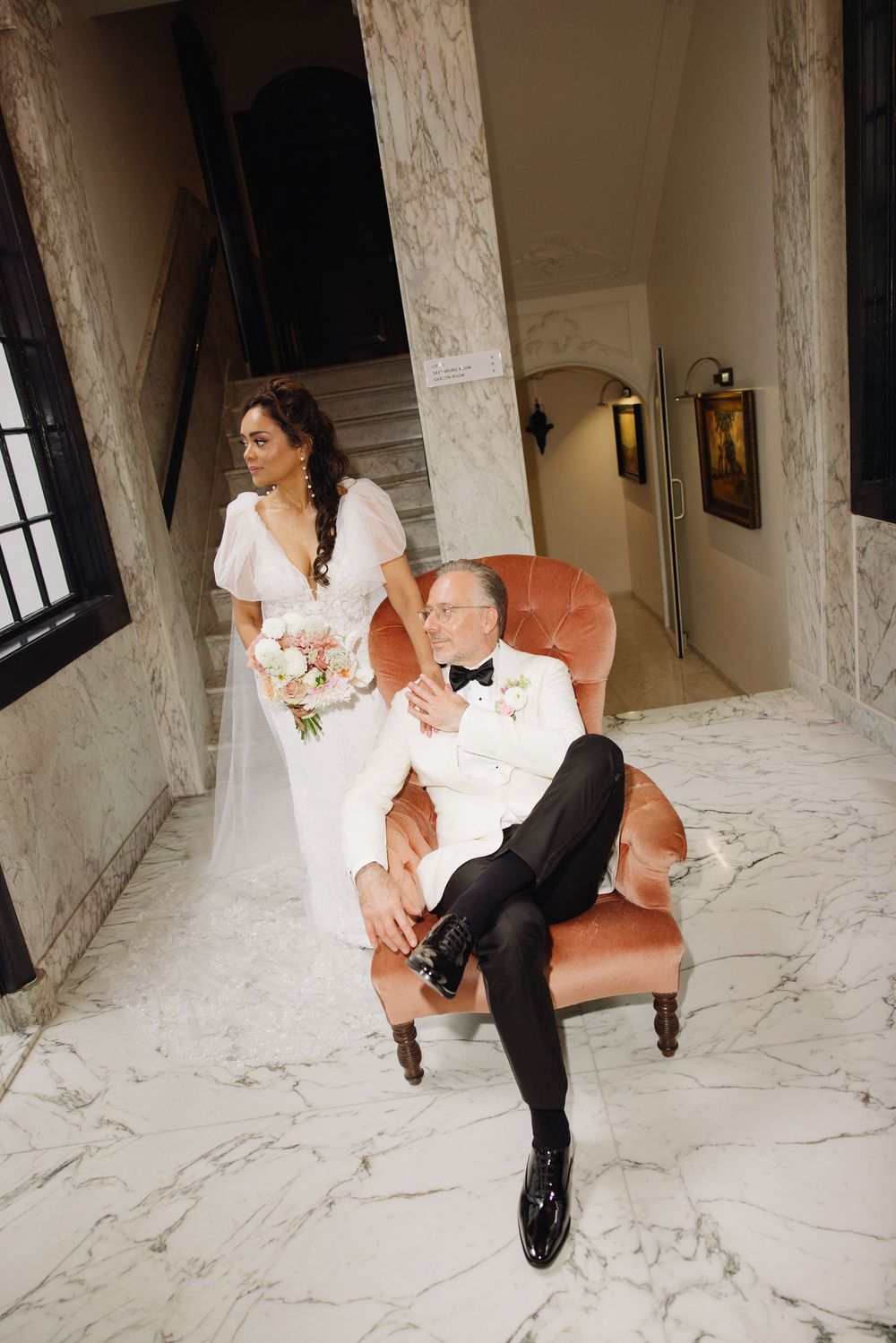 Romantic wedding portraits on a vintage coral chair against marble flooring.