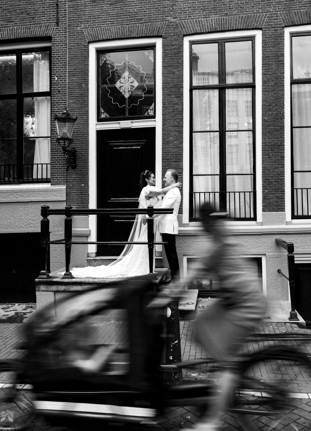 Black and white street scene with motion blur of passing cars on a cobblestone street.