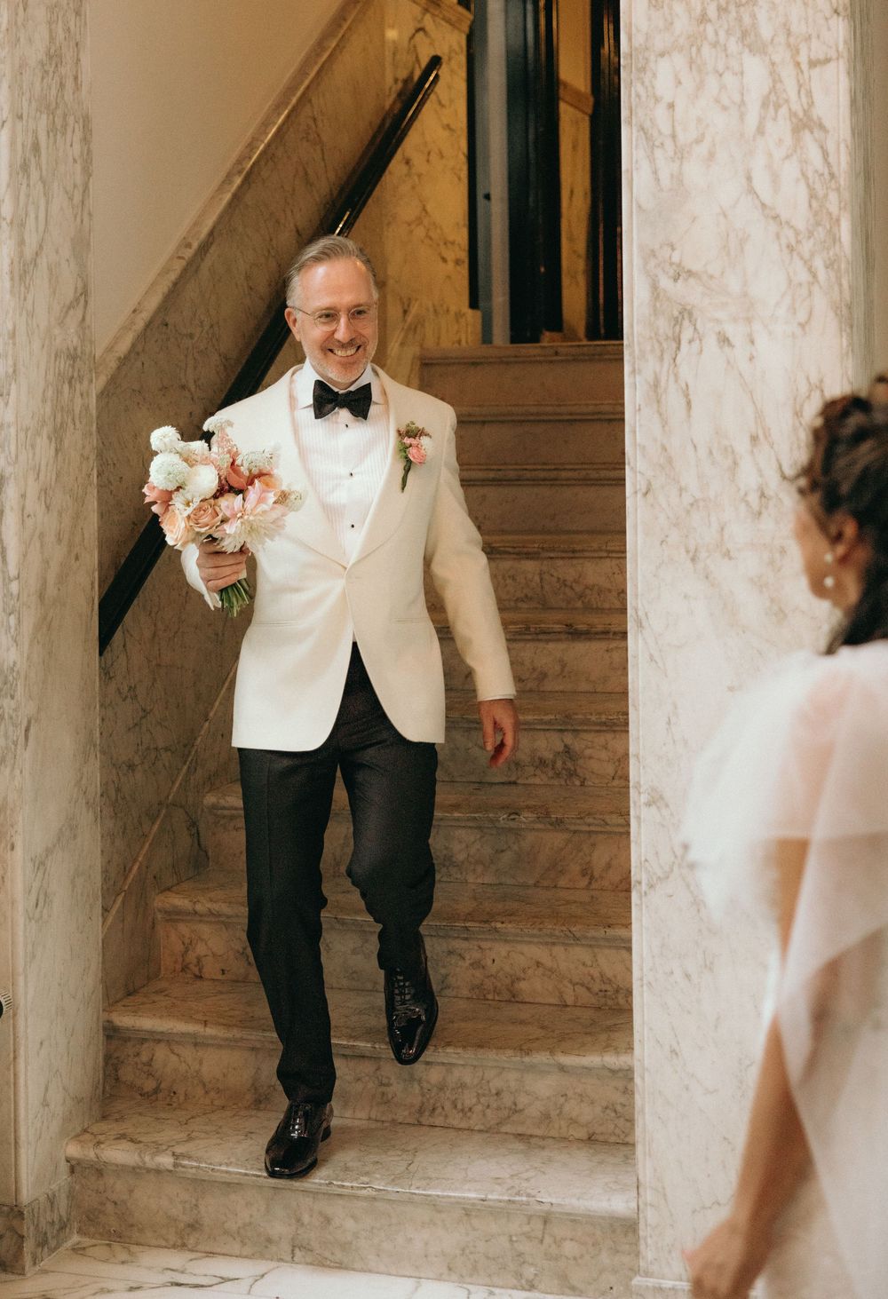 Wedding couple descending elegant marble staircase in formal attire.
