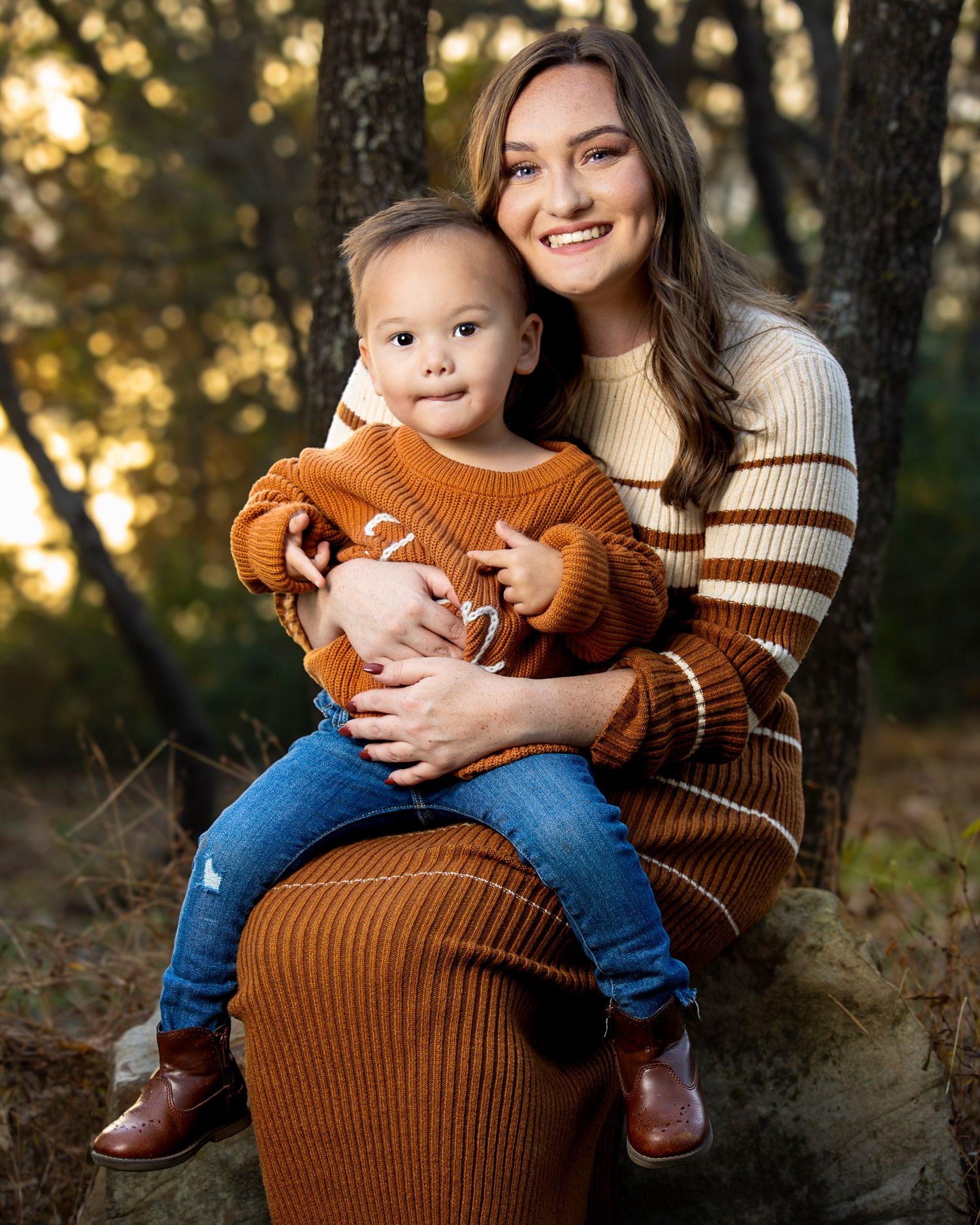 Mother and child in coordinating brown sweaters pose together during an outdoor autumn family photoshoot at Lake Fayetteville.
