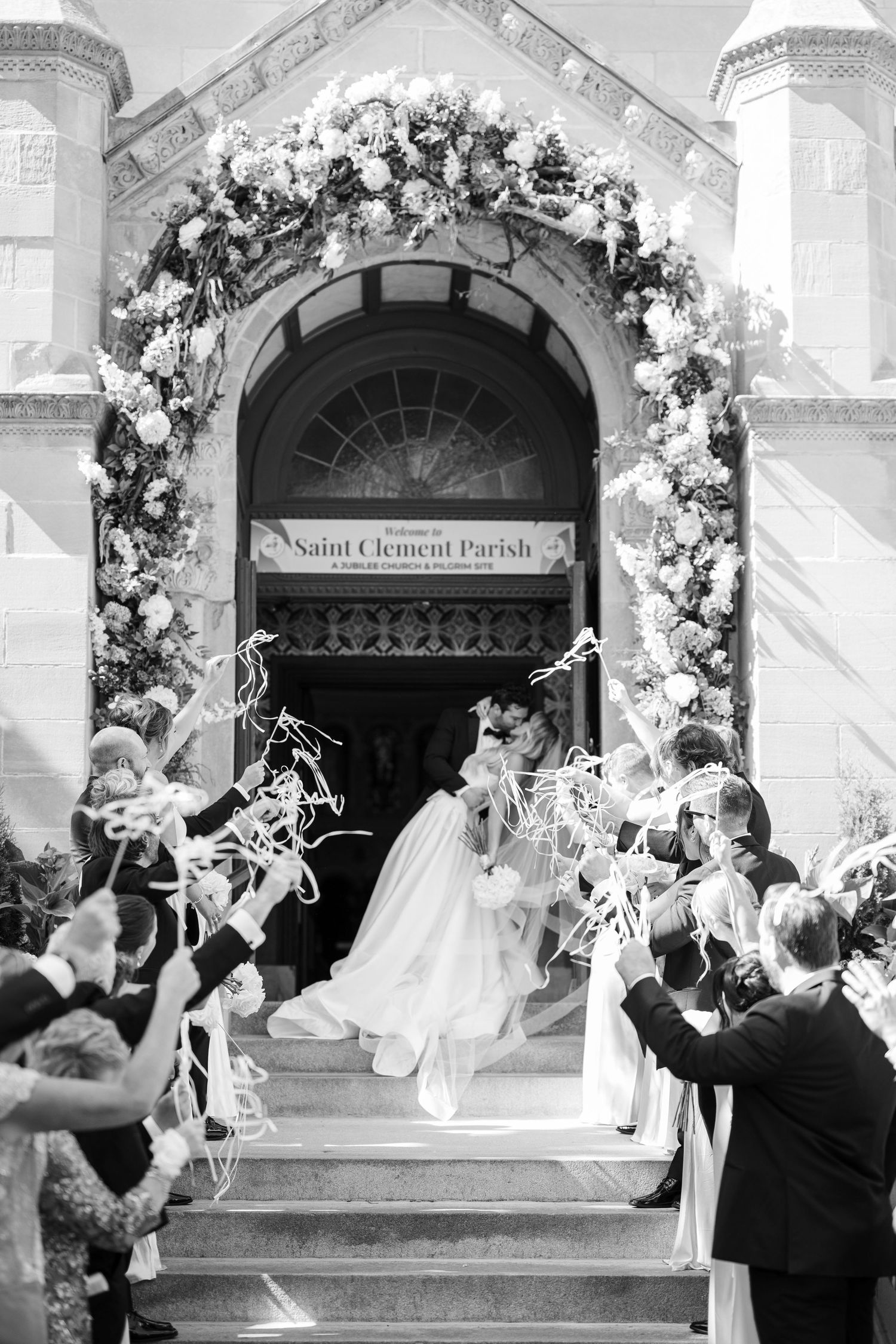 A large group gathers inside an ornate cathedral with domed ceiling for what appears to be a wedding ceremony.