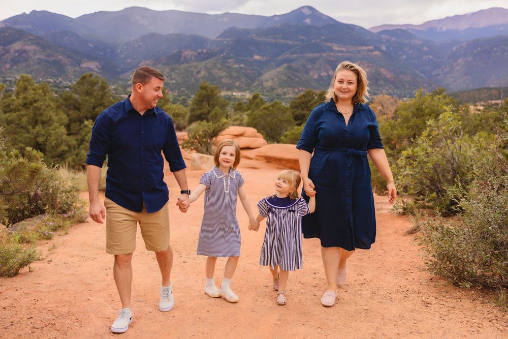 A family walks together holding hands against a backdrop of garden of the gods during sunset.