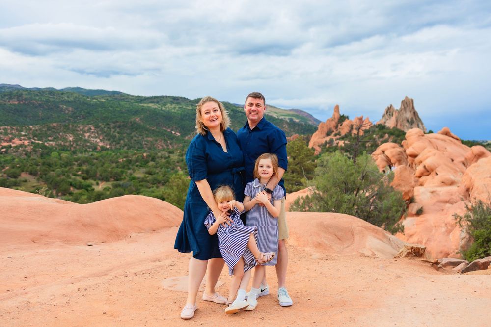 A family poses together on red rock formations at Garden of the Gods park in Colorado during a sunny day.