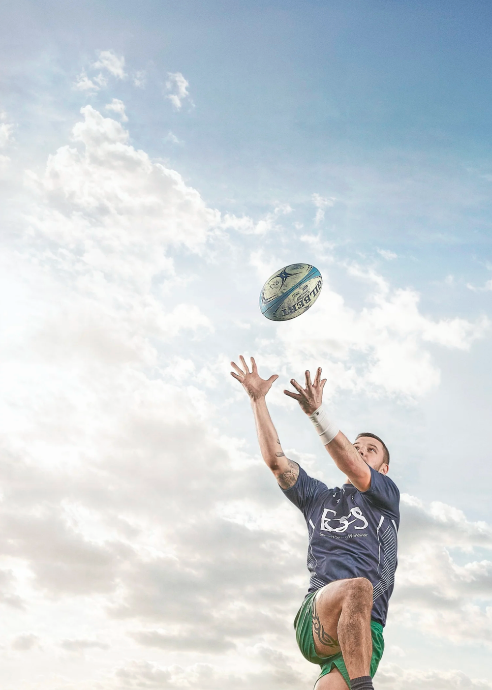 Rugby player jumping to catch ball against cloudy sky.