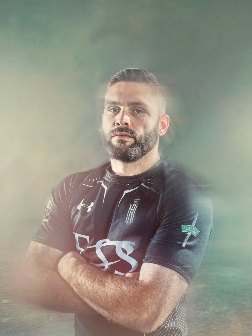 Rugby player in dark uniform stands confidently with crossed arms.