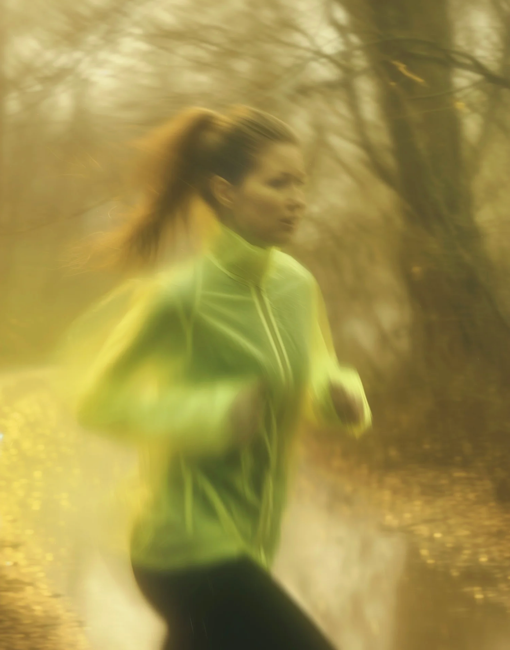 Runner in bright yellow jacket moving dynamically through autumn scenery.